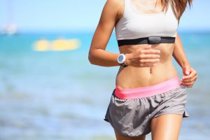 8th International Jerusalem Marathon. Runner woman with heart rate monitor running on beach with watch and sports bra top. Beautiful fit female fitness model training and working out outside in summer at part of healthy lifestyle.
