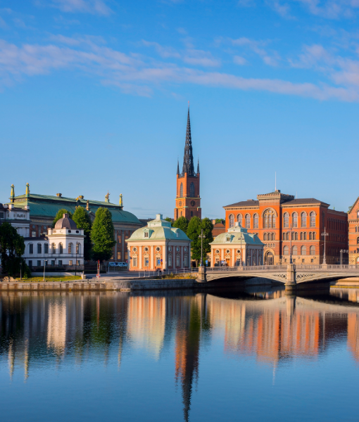 Historic cityscape by a river with a bridge and red-brick buildings, reflected on calm water. - Aufgang Travel
