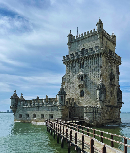 Stone fortress tower standing in shallow water, connected to the shore by a wooden causeway with railings. - Aufgang Travel