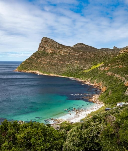 Curved coastline with turquoise water, white-sand beach, and green hills along rocky cliffs under a blue sky. - Aufgang Travel