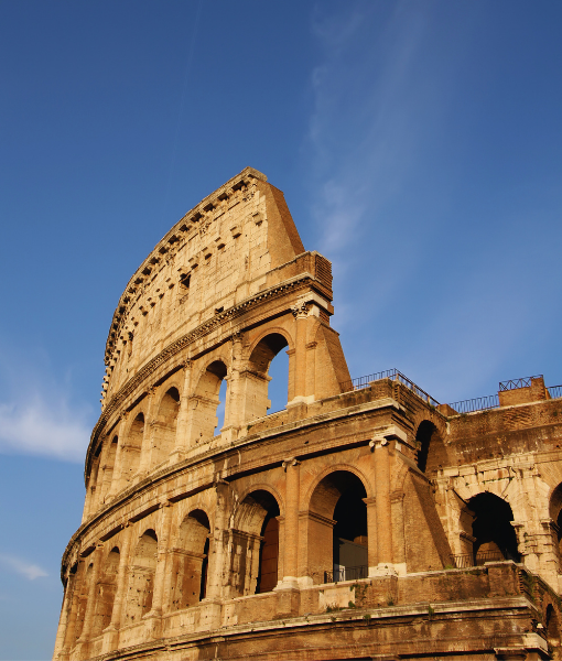 Exterior view of the Colosseum in Rome with arched openings against a blue sky. - Aufgang Travel