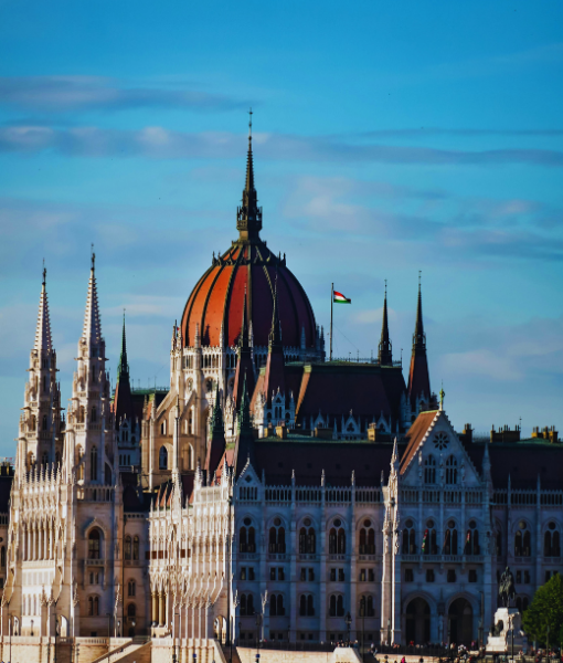 Budapest's Hungarian Parliament Building with its orange-red dome and spires against a blue sky. - Aufgang Travel