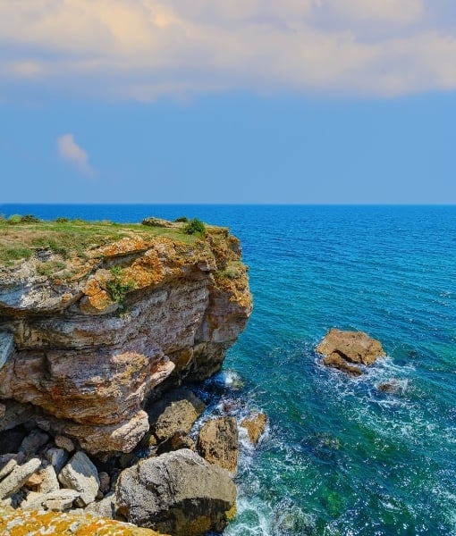 Cliffside rocky coastline overlooking blue sea with waves crashing against rocks. - Aufgang Travel