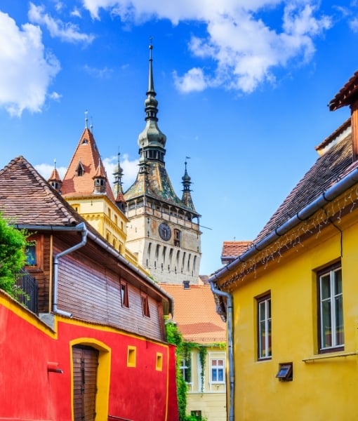 Colorful street in a historic town: red and yellow houses with a tall clock tower against a blue sky. - Aufgang Travel