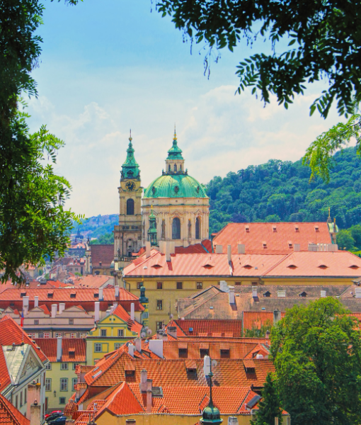Historic European city skyline with red-tiled roofs and a green-domed cathedral framed by trees. - Aufgang Travel