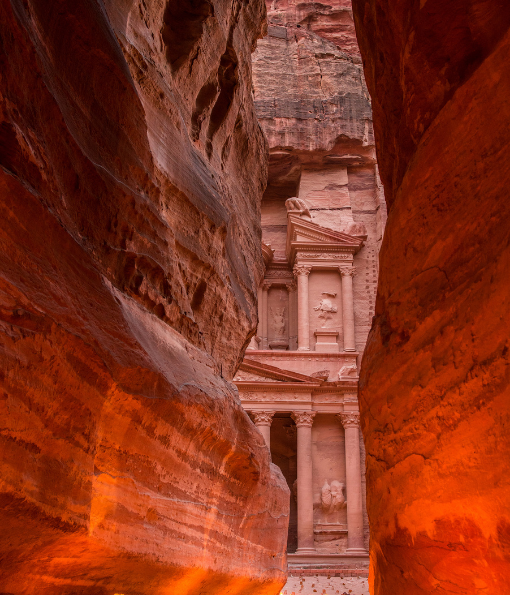 Petra's Treasury facade visible through a narrow red sandstone canyon (Siq). The warm orange walls frame the ancient entranceially carved facade. - Aufgang Travel