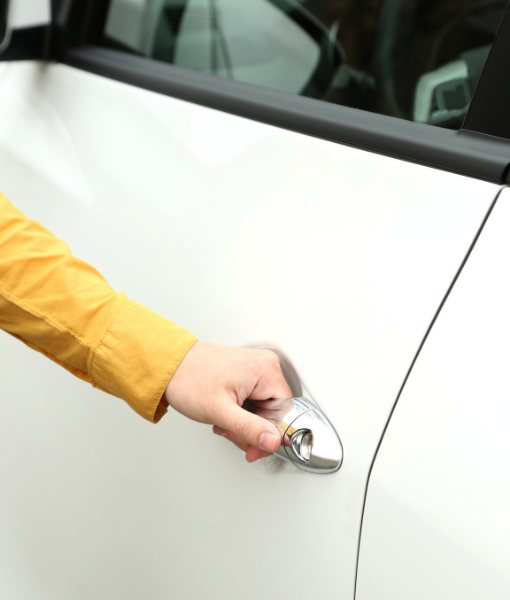 Close-up of a hand in a yellow sleeve gripping the chrome door handle of a white car. - Aufgang Travel
