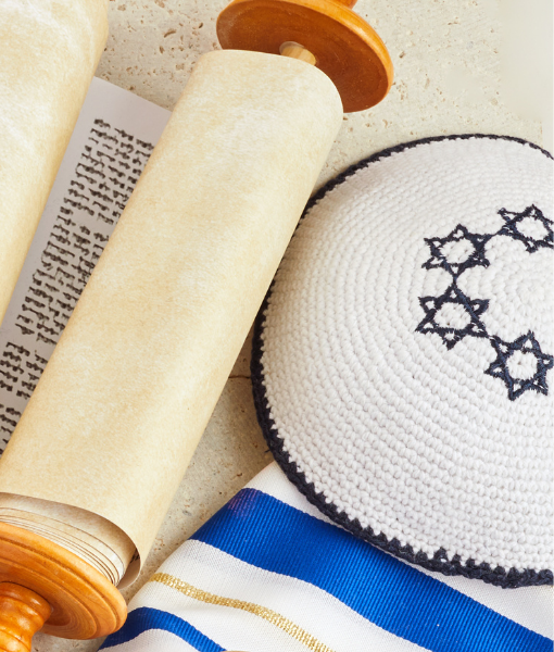 Close-up of a Torah scroll with parchment, a striped tallit, and a crocheted kippah on a light background. - Aufgang Travel