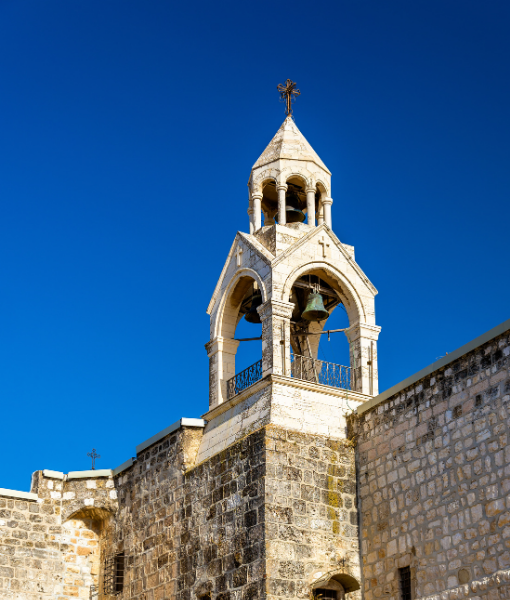 Stone bell tower with arched openings and bells, rising from a fortress wall under a clear blue sky of noon light. - Aufgang Travel