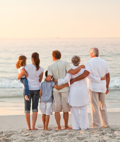 Family of three generations stands on the beach at sunset with arms around each other, facing the ocean. - Aufgang Travel