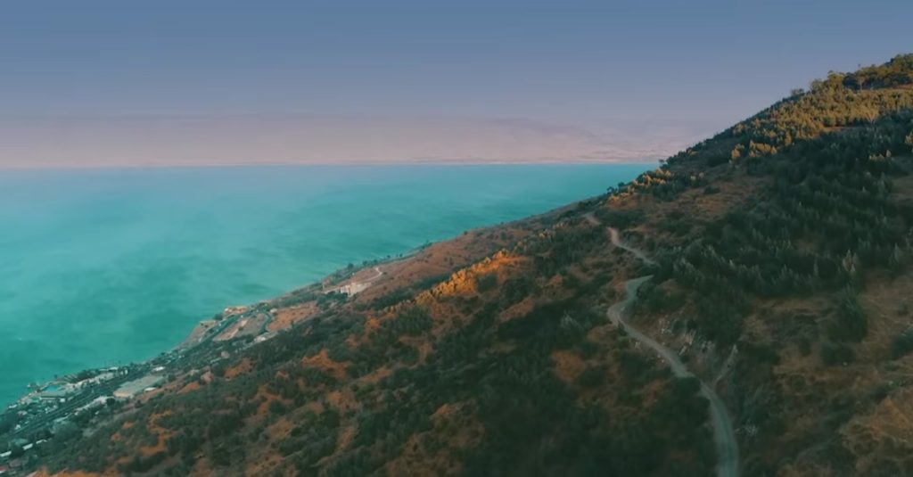 Aerial view of a turquoise sea along a steep hillside with a winding dirt road running down the slope.
